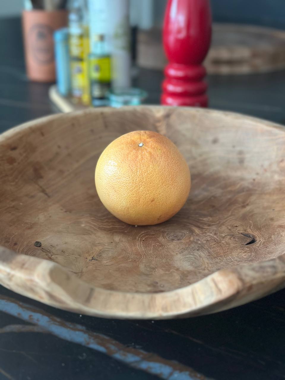 Stor rustik træskål med en grapefrugt på et mørkt køkkenbord