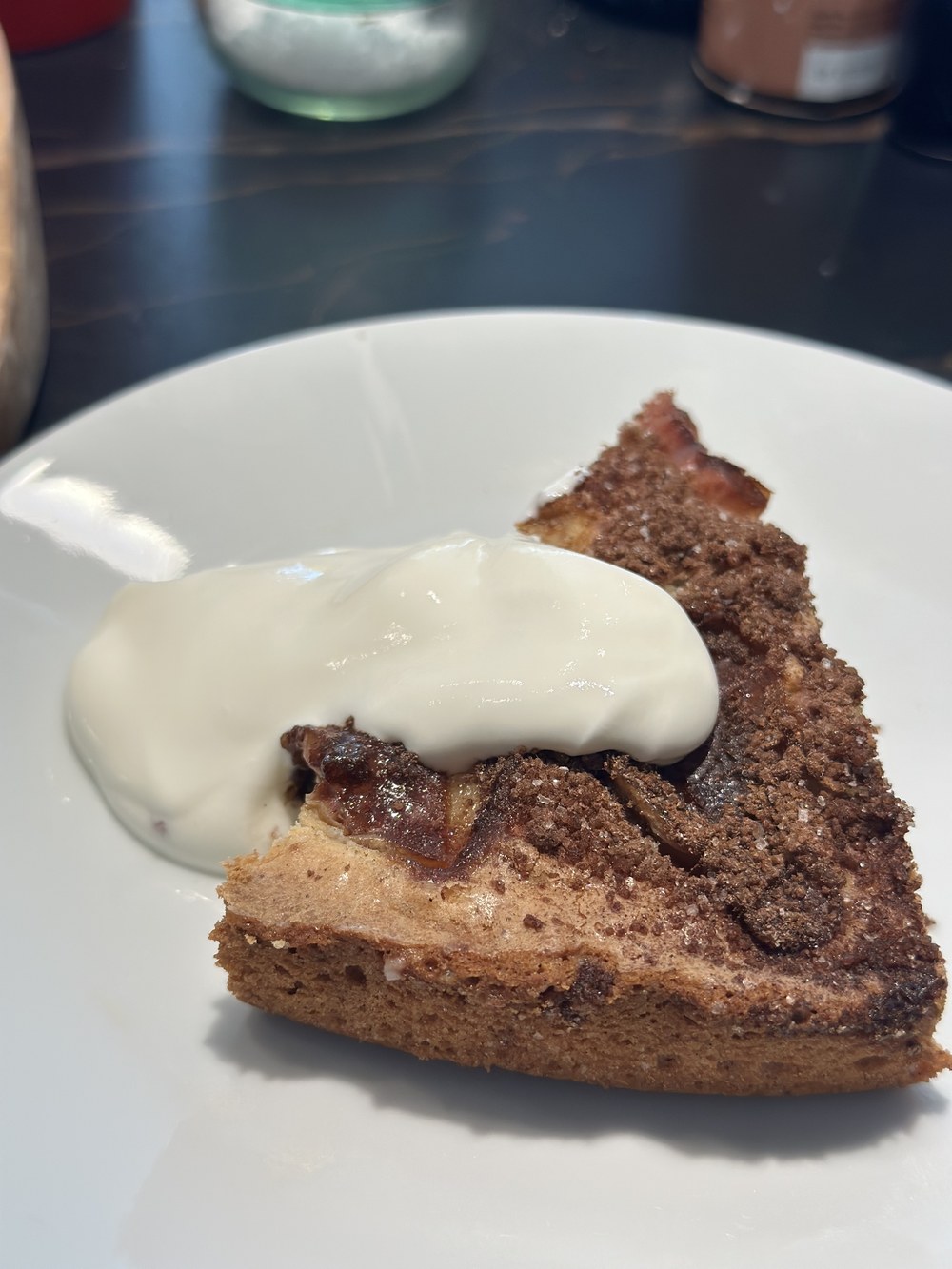 Et stykke æblekage på en hvid tallerken med en klat flødeskum
