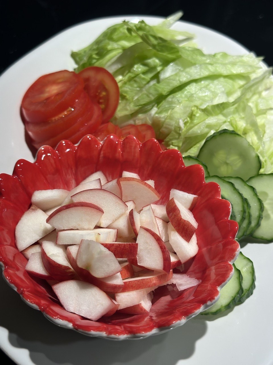 Hakkede røde æbler i en rød skål ved siden af salat, tomat og agurk